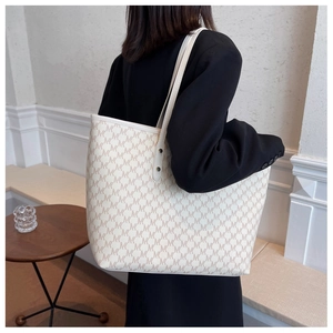 Dettaglio della grande borsa tote beige con stampa monogramma M indossata da modella