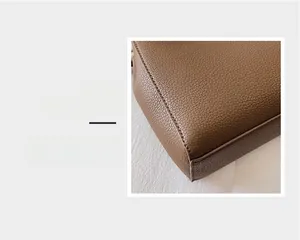 Macro detail of brown leather tote bag showing lychee grain texture and neat stitching
