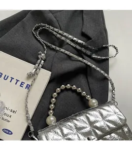 Close-up of silver quilted crossbody bag with pearl beaded handle and metal chain strap