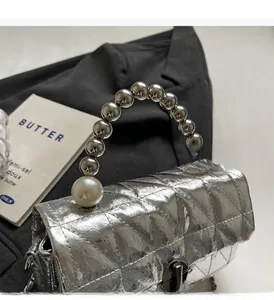 Close-up of silver quilted handbag with metallic fold texture and pearl chain handle