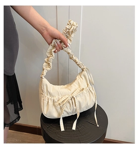 Detail of a beige canvas dumpling bag featuring ruched cloud handle and bow decoration