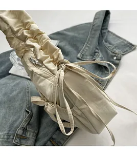 Detail of cream drawstring nylon crossbody bag with pleated strap on denim jacket