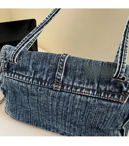 Detailed close-up of blue denim shoulder bag with contrast yellow stitching and metal rings