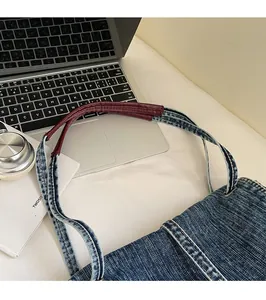 Detail of red leather shoulder strap and metal buckle on blue denim tote bag