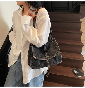 Macro detail of washed black denim shoulder bag with silver buckle on wooden stairs