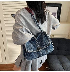 Detailed view of blue denim shoulder bag featuring contrast stitching and metallic lock