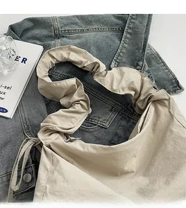 Detail view of beige nylon tote bag with wide pleated strap and side drawstring on denim