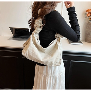 Detailed close-up of a stylish off-white nylon shoulder bag with pleated texture and wide strap