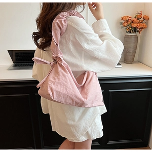 Pink pleated nylon hobo bag shown as a crossbody on a model in a cozy office setting