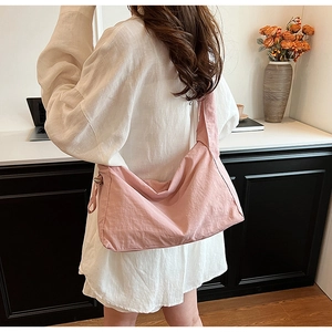 Pink nylon crossbody bag with wide shoulder strap showing back-worn style on model
