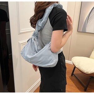 Detail of light blue pleated nylon shoulder bag worn by model in minimalist room