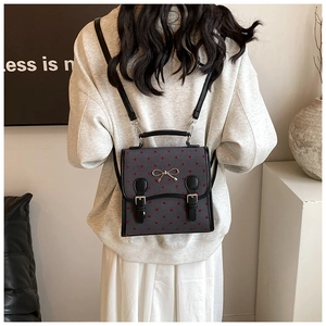 Detailed back view of a grey polka dot backpack with red hearts and a metal bow ornament