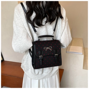 Close-up of black backpack with red heart patterns and silver bow buckle on model