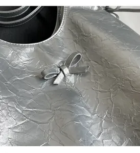 Detail of silver metallic textured fabric and delicate leather bow on the stylish handbag
