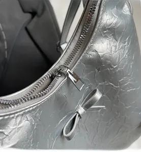 Detail of silver pleated tote bag with smooth metal zipper and side bow accent