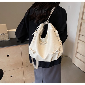 Detail of off-white PU leather crossbody bag featuring textured fabric and decorative bows