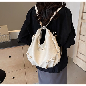 Detail of cream pleated leather backpack with bow accent worn over the shoulder