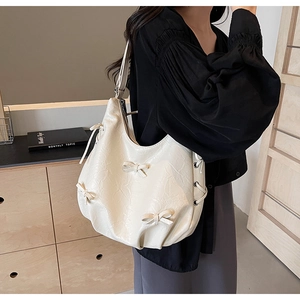 Detail of cream white leather tote bag featuring a decorative bow and textured finish