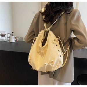 Detail of light yellow pleated backpack with ribbon bow showing soft texture and strap