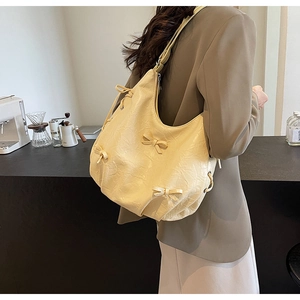 Close-up of creamy hobo bag with bow details and wrinkled texture on a fashion model