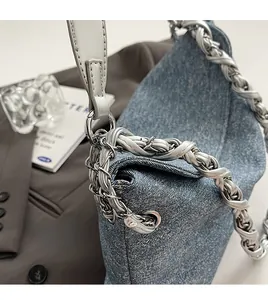 Detailed view of blue denim handbag with elegant silver woven chain strap and metal hardware