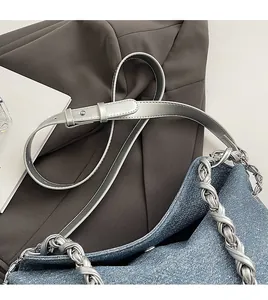 Close-up of denim tote bag featuring adjustable silver leather strap and chunky metal chain