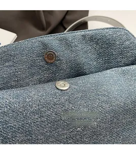 Close-up of metal magnetic buckle and blue denim texture on minimalist crossbody bag