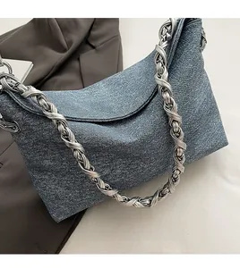 Detail view of denim crossbody bag featuring a thick silver twisted metal chain strap