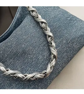Close-up of blue denim bag featuring stylish silver twisted woven metal chain handle