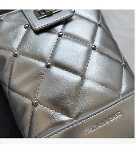 Details einer silbernen Stepptasche mit Metallnieten und geprägtem Logo-Schriftzug