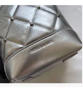 Detailansicht der silbernen Stepptasche mit Metallnieten und eingraviertem Schriftzug