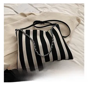 Detail view of striped canvas bag featuring decorative metal chain and leather strap