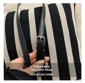 Macro detail of adjustable black leather strap and silver buckle on striped knit tote bag