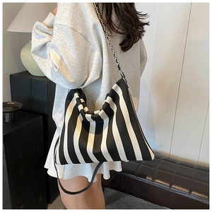 Detailed view of striped canvas tote bag with chain strap shown on person in modern interior