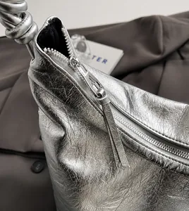 Detail of silver metallic tote featuring a smooth zipper and unique knotted handle