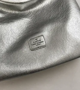 Detail of silver metallic textured tote bag featuring an embossed brand logo and ribbon
