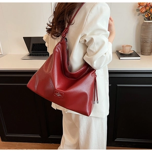 Detail of burgundy leather tote bag featuring knotted strap and side tassel zipper accent