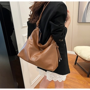 Detail showing caramel brown leather hobo bag with unique knot design and brand logo