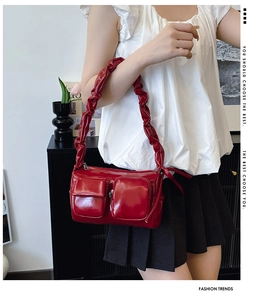 Detail of red patent leather handbag featuring glossy finish and ruched shoulder strap