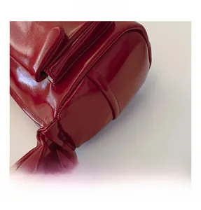 Detail of burgundy glossy leather handbag showing pleated handle texture and precise stitching