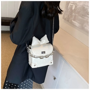Detail van witte mini crossbodytas met strikdecoratie en dikke metalen ketting