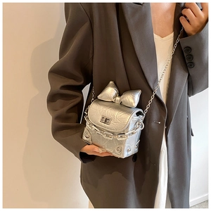 Detailopname van zilveren crossbodytas met grote strik en grove metalen ketting