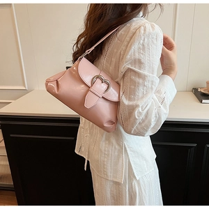 Gros plan d'un sac selle rose brillant avec boucle cœur en argent et détails plissés
