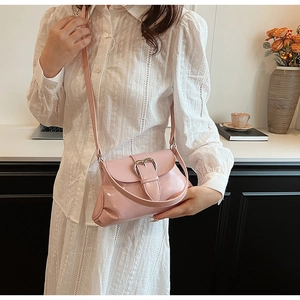 Detail of pink patent leather shoulder bag with a silver heart-shaped metal buckle on model