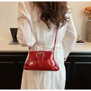 Detail of red glossy saddle bag featuring a heart-shaped metal buckle and chic ruched texture