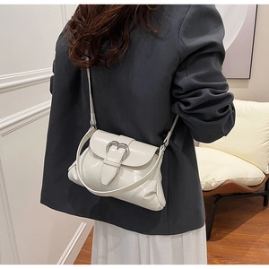 Detail view of a white saddle bag with a silver heart buckle on a fashion model