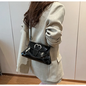 Detail of glossy black saddle bag with a large silver heart buckle on a beige suit