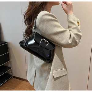 Vue latérale du sac à bandoulière noir brillant avec boucle cœur argentée sur un blazer