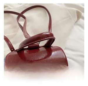 Detail of glossy wine red embossed leather handbag with top handle and thin strap