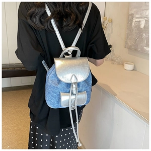 Mini backpack in blue denim and silver leather shown on back in a minimalist setting
